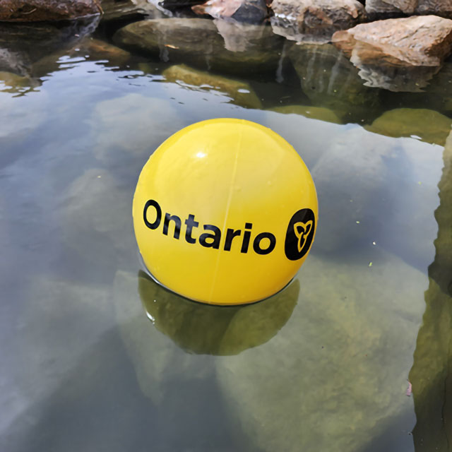 A yellow buoy with the Ontario government logo in black floats on the surface of a lake. 